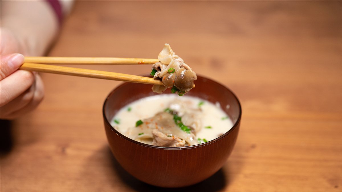 豚肉ときのこ、ねぎが入った具だくさんの豚汁を箸で持ち上げているところ