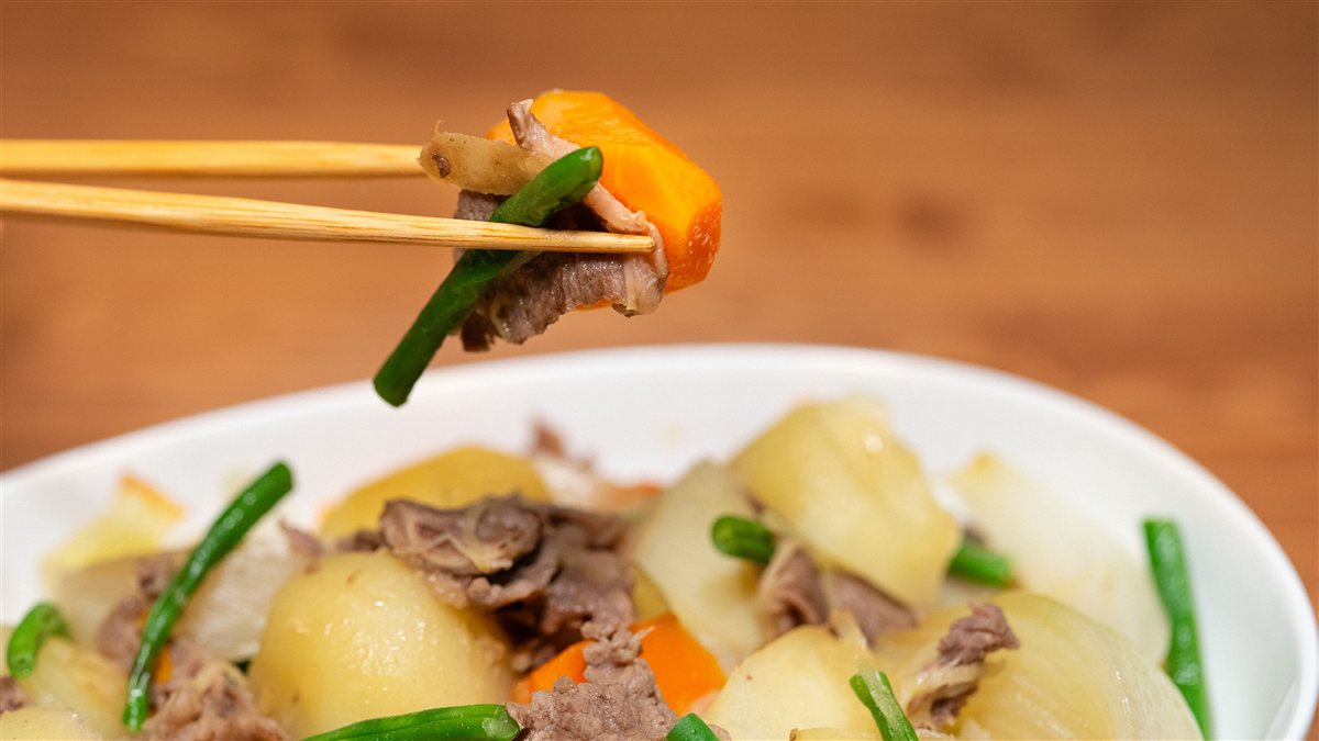 箸でつまんだ肉じゃがの具材と、白い器に盛られた肉じゃが